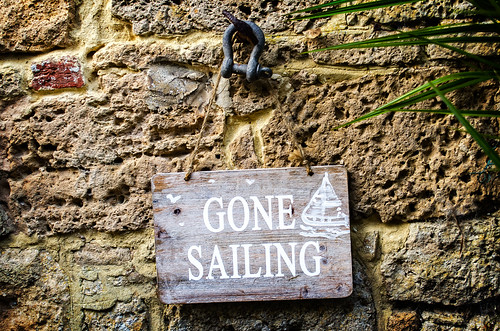 A wooden sign saying "gone sailing" on an old stone wall